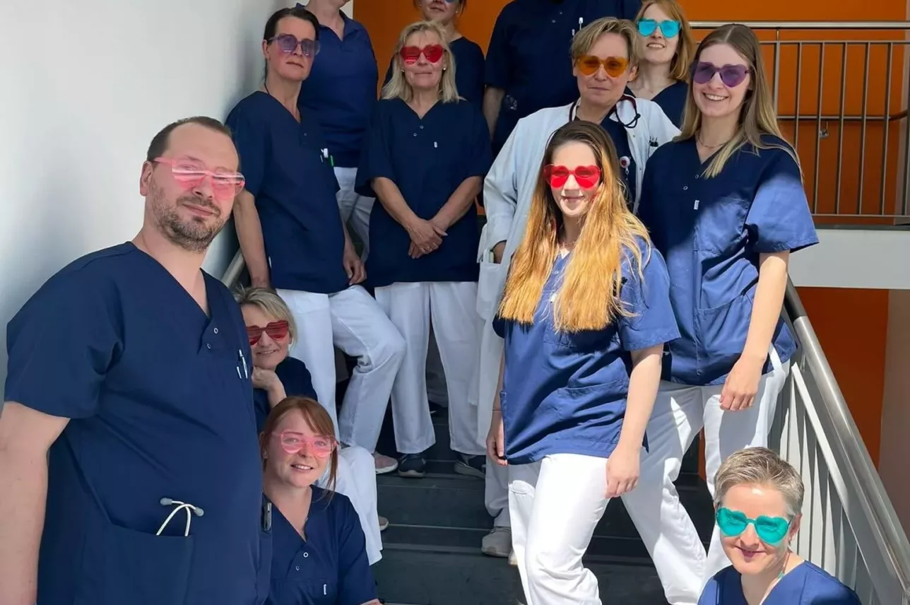 Das Team der Nephrologie des Johannes Wesling Klinikums posiert mit bunten, herzförmigen Sonnenbrillen auf einer Treppe.